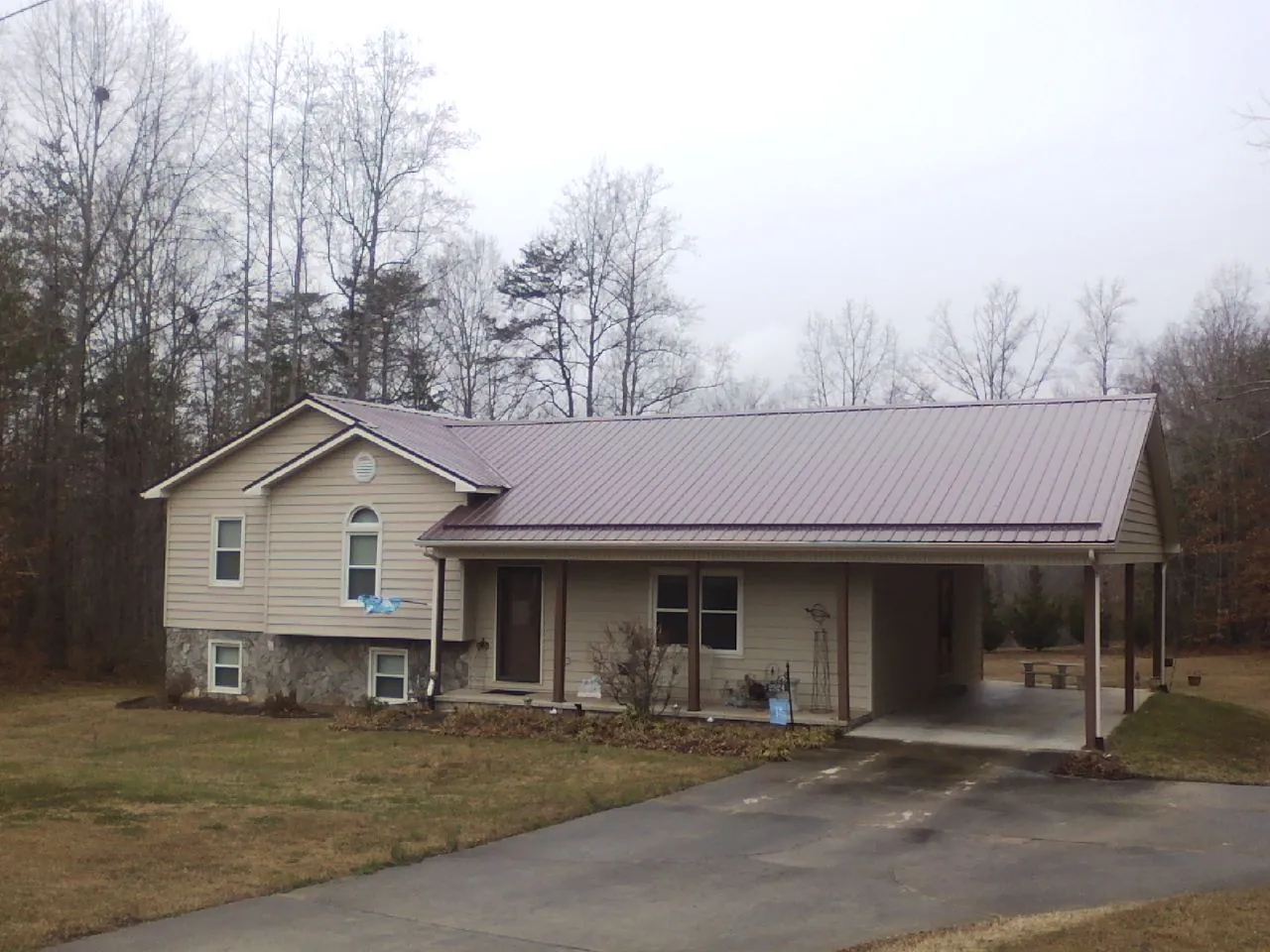 Burgundy metal roof on a tan split level home with an attached carport in Alpine